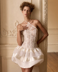 Woman wearing a white lace dress against an ornate wall.